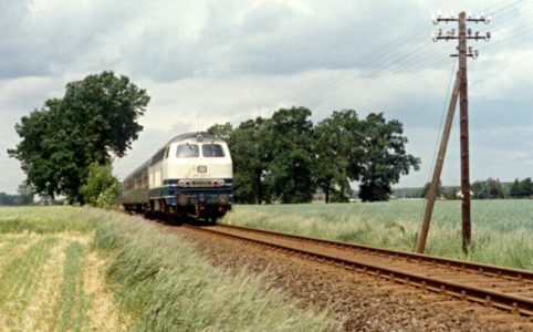 Ein Zug durchfährt bei Xanten eine Landschaft mit Feldern und Bäumen im Hintergrund. Lok ist 215 021